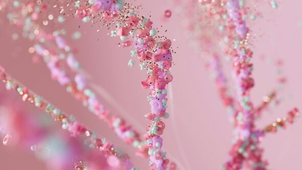 Abstract 3D illustration of intertwined strands composed of glossy pink, purple, cyan, and gold particles, resembling DNA or neural pathways, set against a soft pink background.