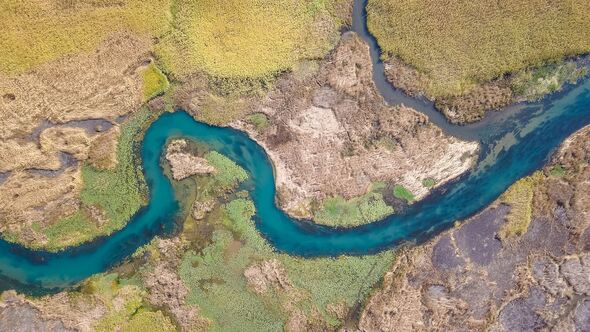 Aerial view of a winding turquoise river flowing through marshland wetlands
