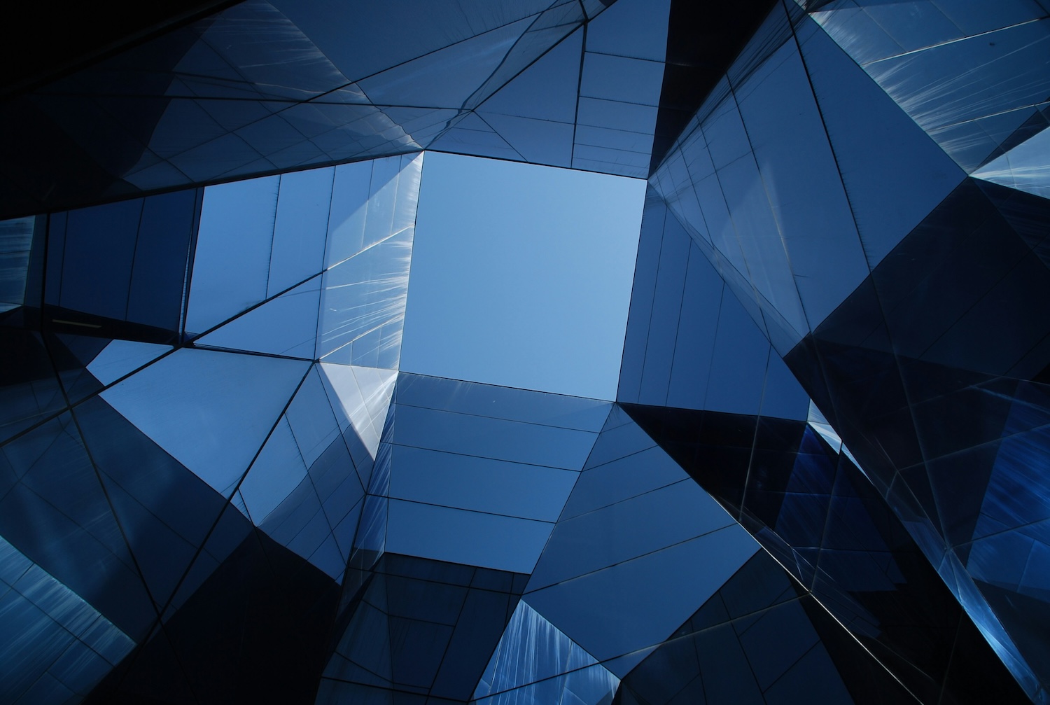 upward view of a modern glass building forming geometric shapes around an open square of blue sky