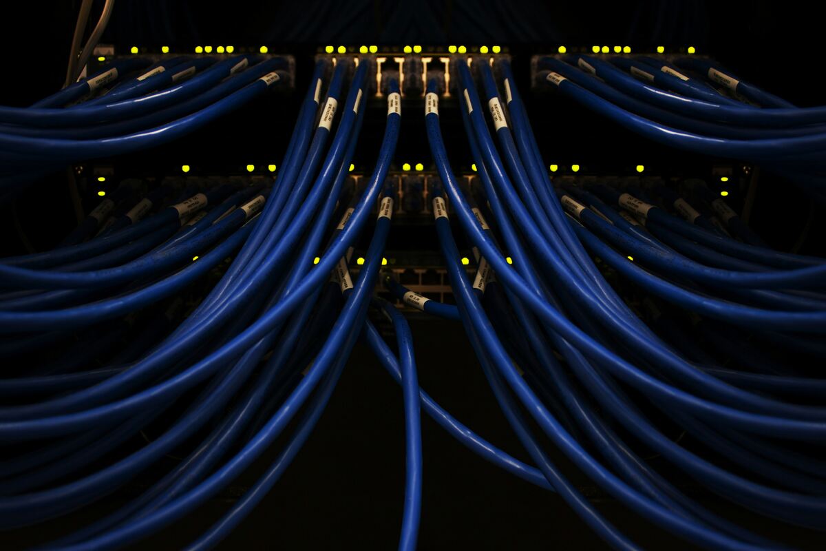 Close-up of blue Ethernet cables connected to a network server, with glowing LED indicator lights in a dark, high-tech environment.